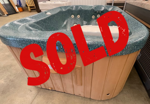Blue speckled hot tub on display in a showroom with built-in jets and seating, marked SOLD with a large red stamp across it