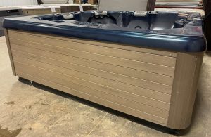 r397 1 | Young's Hot Tub Sales and Service Center A navy-blue hot tub with a wooden paneled exterior sits in a showroom, showing seating and built‑in controls along the inner rim.