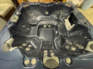 r397 3 | Young's Hot Tub Sales and Service Center Dark blue hot tub interior with multiple massage jets along curved seats, built-in headrests, and control panels in a workshop-like setting.