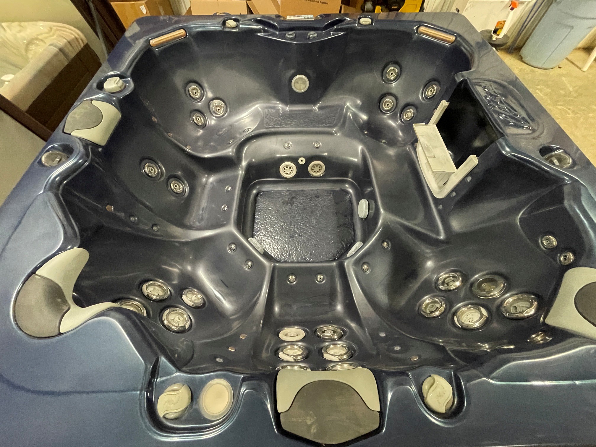 r397 3 | Young's Hot Tub Sales and Service Center Dark blue hot tub interior with multiple massage jets along curved seats, built-in headrests, and control panels in a workshop-like setting.