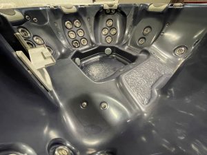 r397 7 | Young's Hot Tub Sales and Service Center View of a dark gray hot tub interior filled with multiple water jets along the seats and walls, showing molded seating and a wet textured floor edge.