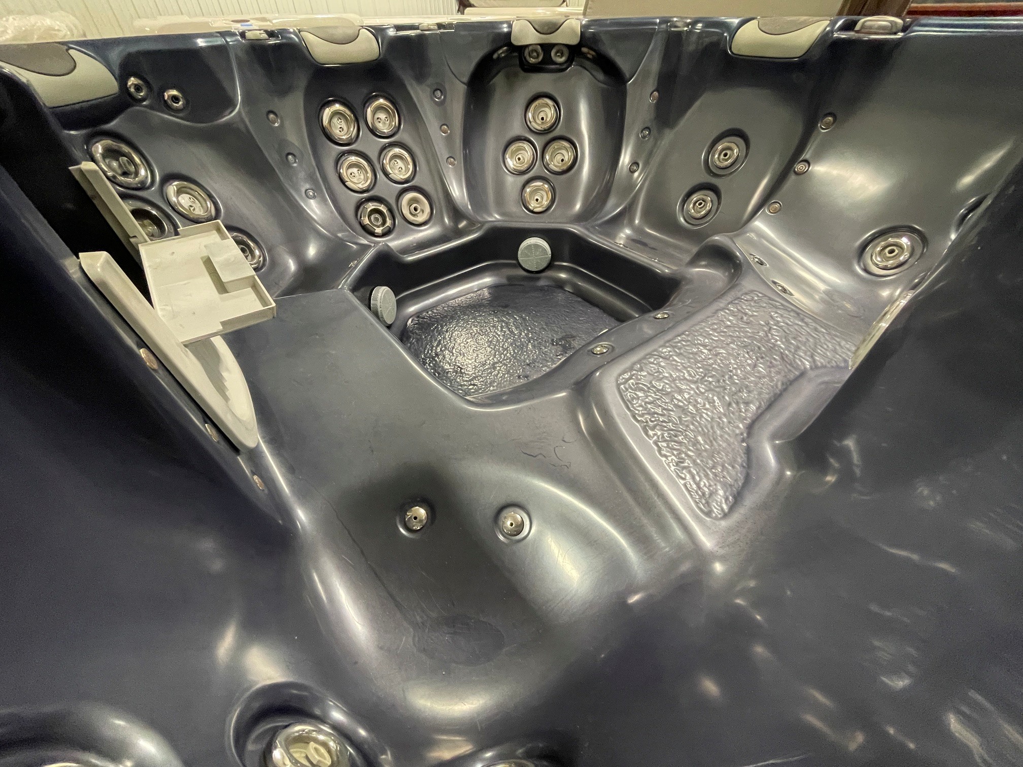 r397 7 | Young's Hot Tub Sales and Service Center View of a dark gray hot tub interior filled with multiple water jets along the seats and walls, showing molded seating and a wet textured floor edge.