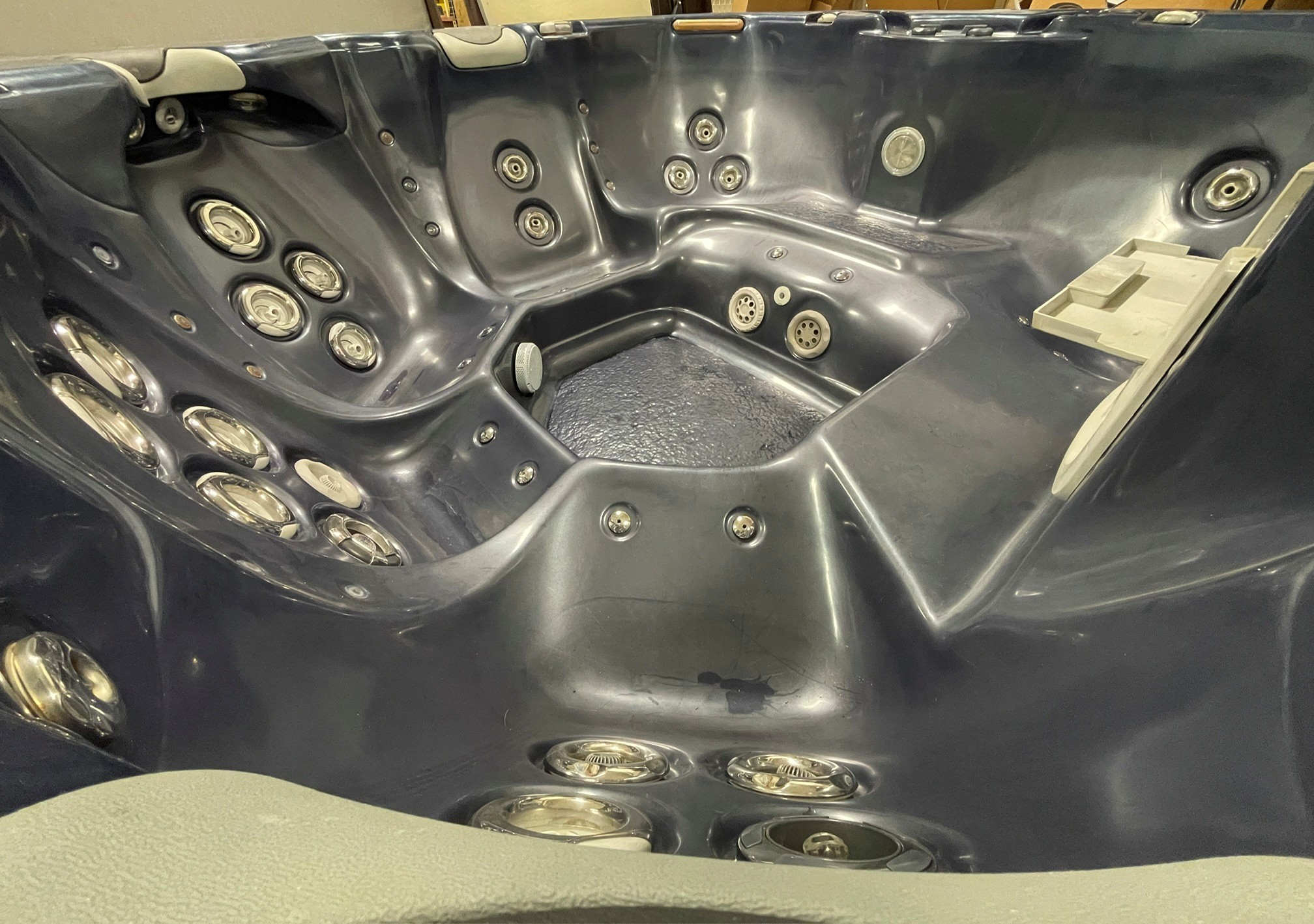 r397 8 | Young's Hot Tub Sales and Service Center Interior of a dark gray hot tub with numerous circular jets along the walls and curved seating areas, empty and awaiting use