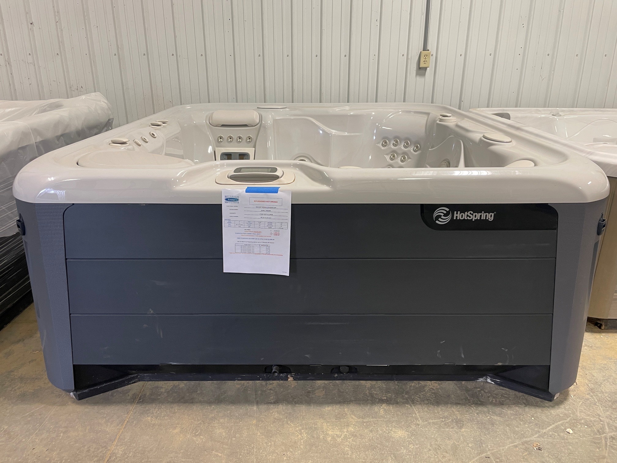 r408 1 | Young's Hot Tub Sales and Service Center White HotSpring hot tub in a showroom with protective plastic cover and a spec sheet taped to the front panel