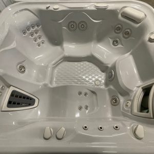 Top-down view of a white hot tub with multiple massage jets and built-in seats, showing a textured floor and control panel on the rim