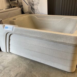 Gray textured hot tub in a showroom, with a built-in control panel on the side and a brochure inserted in a holder nearby.