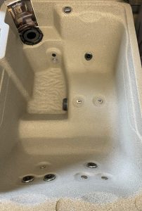 r442 3 | Young's Hot Tub Sales and Service Center Interior of a beige spa tub with built-in seating, multiple jets, and a user manual resting by the edge.