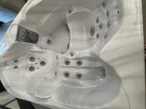 White acrylic hot tub with many circular jets and built-in seating, viewed from above.