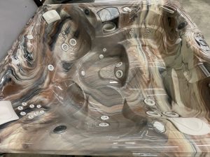r441 4 | Young's Hot Tub Sales and Service Center Marbled brown hot tub interior with numerous circular jets and built‑in controls, covered in protective plastic wrap.