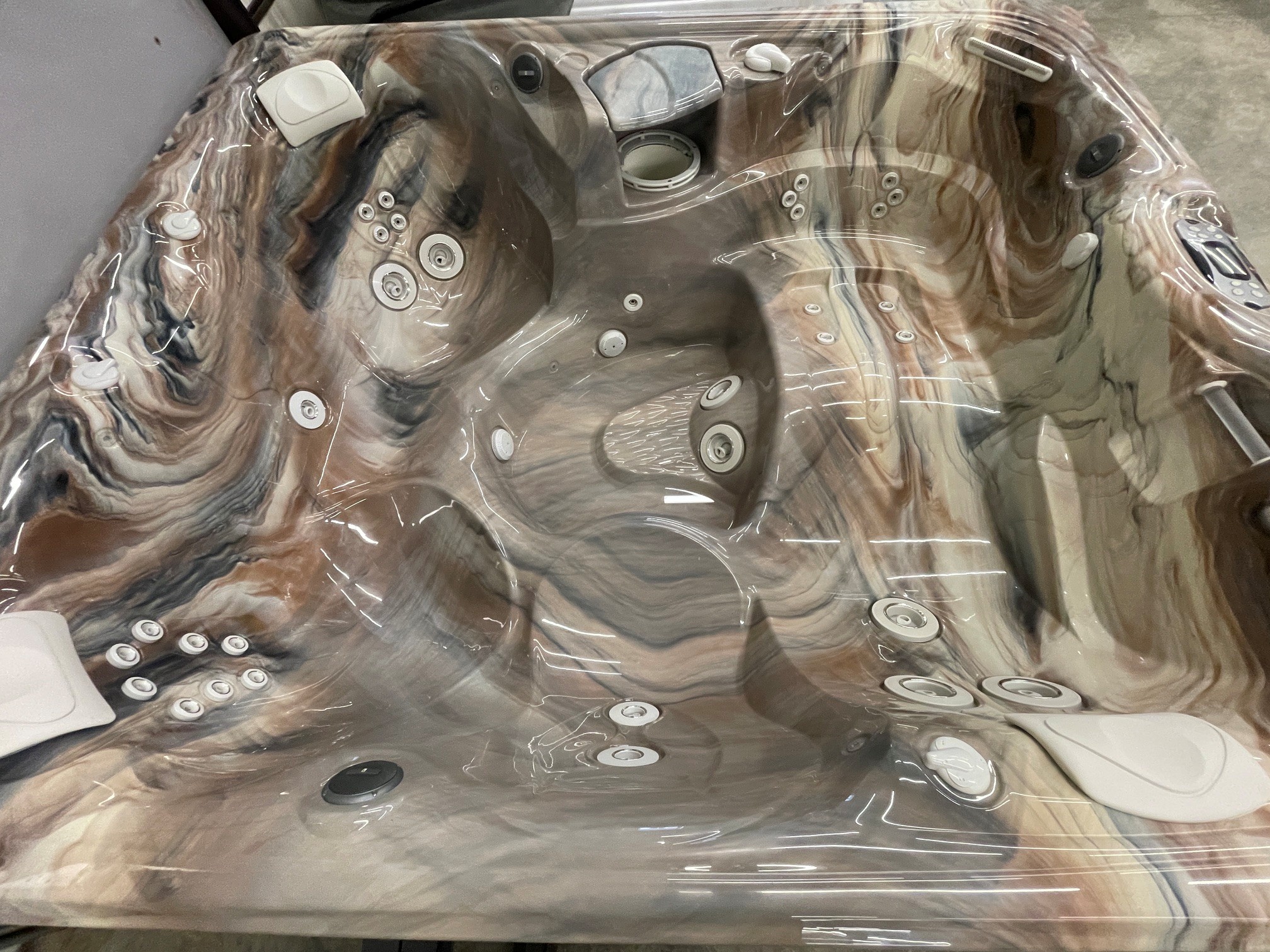 r441 4 | Young's Hot Tub Sales and Service Center Marbled brown hot tub interior with numerous circular jets and built‑in controls, covered in protective plastic wrap.